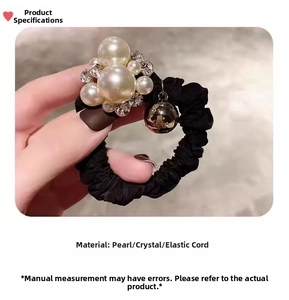 Detail of black elastic hair tie with white pearls, crystals and a small gold bell