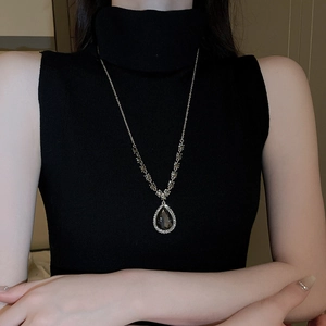 Detailed close-up of a silver necklace with a large pear-shaped dark gemstone and diamonds