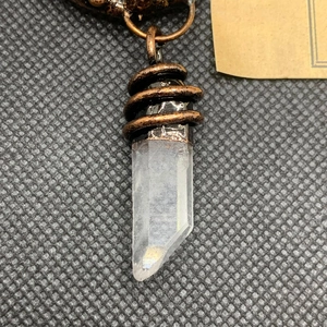Close-up of hexagonal crystal pendant with bronze wire wrap on textured background