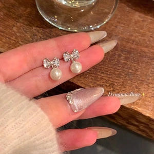 Detailed view of silver bow earrings with micro-set zircons and a round white pearl drop