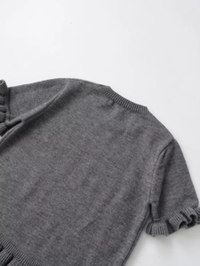 Detail of grey knitted top featuring ruffled hem and ribbed flutter sleeve texture