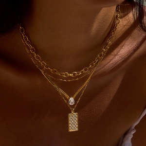 Close-up of a layered gold titanium steel necklace with square and drop pendants on model