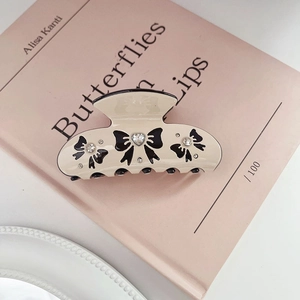Detailed close-up of beige hair claw clip with black bow pattern and sparkling rhinestones