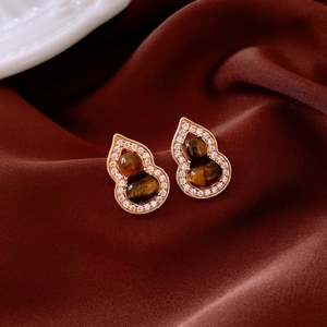 Détail de boucles d'oreilles gourde en or avec œil de tigre et cristaux sur velours