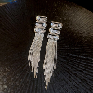 Detail of silver tassel earrings with geometric zircon stones on a dark textured background