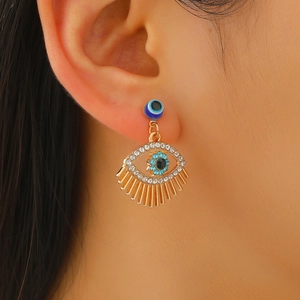 Detail of golden Evil Eye stud earring with blue crystals and fringe tassels on ear
