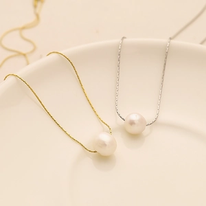 Détail de pendentifs en perles sur chaînes en or et argent posés sur une assiette en céramique