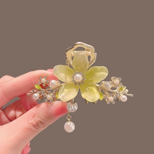 Détail de pince à cheveux fleurie avec cadre doré, pétales translucides et pompons perles