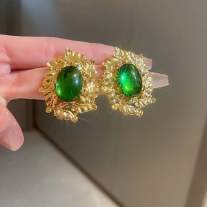 Detail of vintage gold earrings with large oval green gemstone in leafy filigree