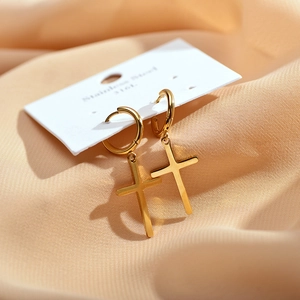 Close-up of gold stainless steel cross pendant earrings on elegant orange silk fabric
