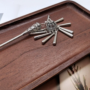 Detail of silver tassel hair stick with retro hollow design on a dark wood tray