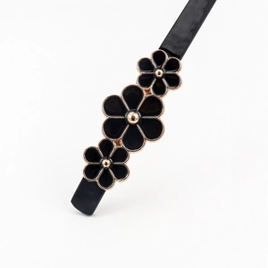Detail of a thin black belt featuring three black and gold decorative floral accents