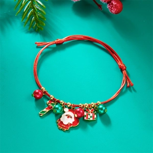Detail of red braided Christmas bracelet with Santa and candy cane charms on green background