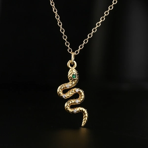 Golden snake pendant necklace with green gemstone eyes and white stones on a gold chain