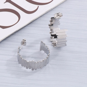 Vue macro de boucles d'oreilles créoles en acier argenté avec texture ondulée sur tissu