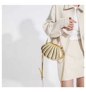 Detailansicht einer metallisch goldenen Muschel-Umhängetasche mit elegantem Perlengriff