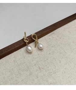 Macro detail of gold knot earrings with freshwater pearls on a minimalist wooden stand