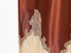 Macro detail of silk-textured satin skirt featuring delicate lace trim and copper finish