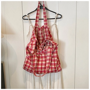 Detail shot of a red and beige checkered tote bag on a hanger with white dress background