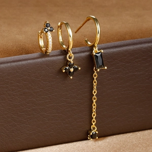 Detail of three gold earrings with black stones and clover charms on a leather box
