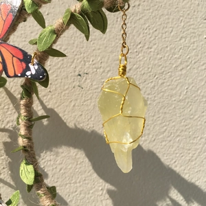 Macro detail of natural yellow crystal pendant wrapped in gold wire on a branch