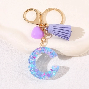 Detail of letter C resin keychain with purple tassel, heart charm, and golden metal clasp