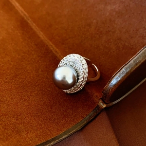Macro detail of silver-tone oval pearl ring with zircon accents on brown velvet surface
