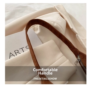 Detail of wide suede strap and metal zipper on brown shoulder bag with blazer background