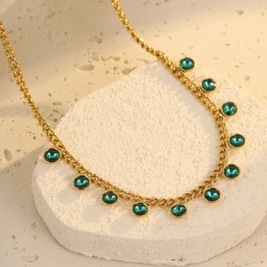 Detailed macro view of a gold chain necklace with eleven round green gemstones on white stone
