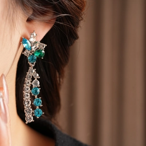 Macro view of silver tassel earrings with blue and green rhinestones on a female model