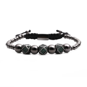 Dettaglio macro del bracciale con perle nere, zirconi verdi e cordino intrecciato