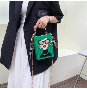 Detail of green hard-shell box bag featuring an artistic relief face and printed silk scarf