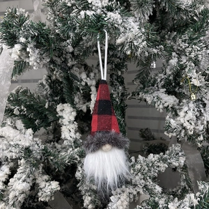 Christmas gnome ornament in red black plaid hanging on a snowy tree branch