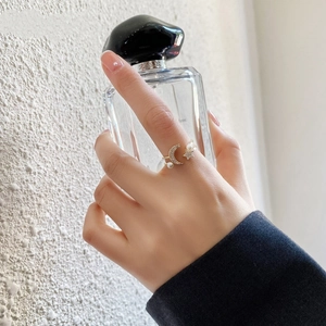 Anello aperto dorato con luna, stella, zircone e perla indossato con boccetta di profumo