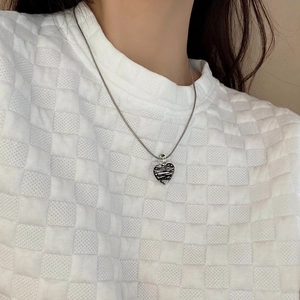 Detail shot of a silver heart pendant with unique wavy texture on a fine snake chain