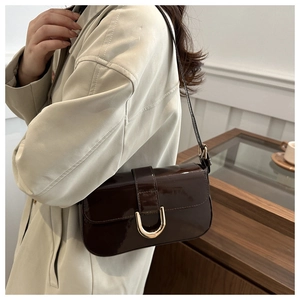 Deep brown patent leather shoulder bag with horseshoe buckle shown on a model