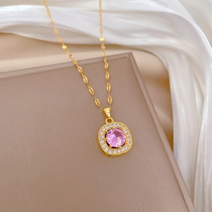 Detail of square gold necklace with a pink gemstone pendant on a beige jewelry box