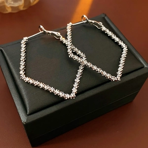 Detailed close-up of silver geometric hoop earrings with textured metal weave design