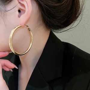 Close-up of elegant large gold hoop earrings worn with a professional black suit outfit