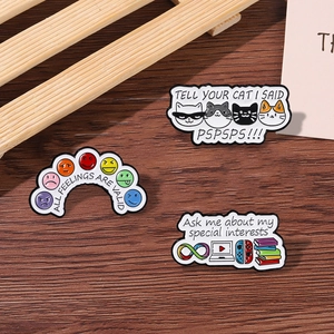 Detailed close-up of three metal enamel pins with creative slogans on a wood surface