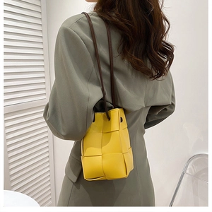 Detail view of yellow hand-woven bucket bag styled with a grey blazer for women