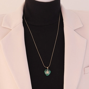 Detail of green malachite heart pendant on gold chain worn with a beige blazer