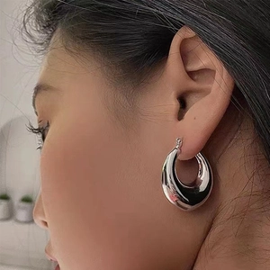 Close-up of a chunky hollow teardrop earring in polished silver finish on a model