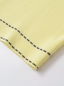 Detail of yellow knit cardigan showing textured fabric and black dashed trim accents