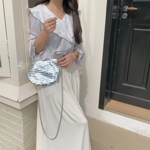 Detail of silver sequin handbag with metal chain strap shown in a fashion lifestyle setting