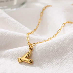 Close-up of gold 3D letter pendant with beaded texture on elegant white fabric
