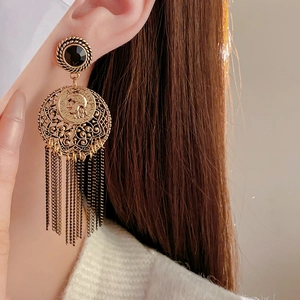 Detailed close-up of gold tassel earring with black gem and vintage coin on model