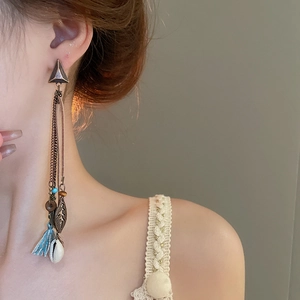 Detail of bohemian tassel earring with bronze leaf, blue fringe and shell on model