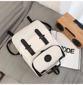 Flat lay of a white canvas backpack with black straps next to a magazine and speaker