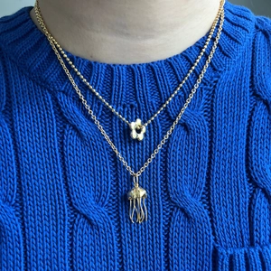 Golden double layer necklace featuring flower and jellyfish pendants on a blue sweater